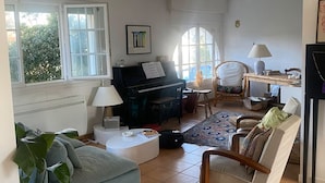 Ein Wohnzimmer mit einem Klavier, einem Sofa, einem Sessel, einer Lampe und einem großen Fenster.