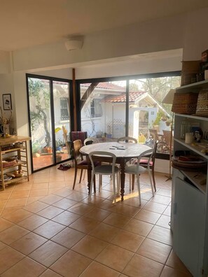 Ein Essbereich mit einem runden Tisch und Stühlen, einem Regal mit Körben und Blick durch eine Glastür auf eine Außenpatio.