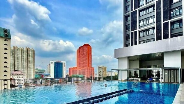 Une piscine au sol carrelé, entourée de bâtiments modernes, dont une haute structure rouge.
