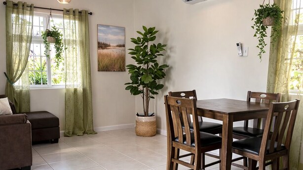 A dining area with a wooden table and chairs, a potted plant, and a painting on the wall.