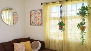 A living room with a brown sofa, yellow and white cushions, a round mirror, and two wall-mounted paintings.
