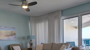 Un salon doté d’un ventilateur de plafond, d’un canapé, d’une table basse et offrant une vue sur l’extérieur grâce à une grande fenêtre.