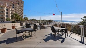 Une terrasse avec des sièges extérieurs, offrant une vue sur une plage et un bâtiment.