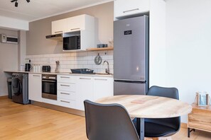 A modern kitchen with a stainless steel refrigerator, microwave, and oven, a wooden dining table with chairs, and a washing machine. - Sleek Sanctuary in the Sky (Cape Town)