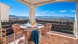 A balcony with a table set for dining, overlooking a scenic landscape. - Vhouse (Badesi)