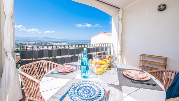 A covered outdoor dining area with a table set for two, overlooking a scenic view. - Vhouse (Badesi)