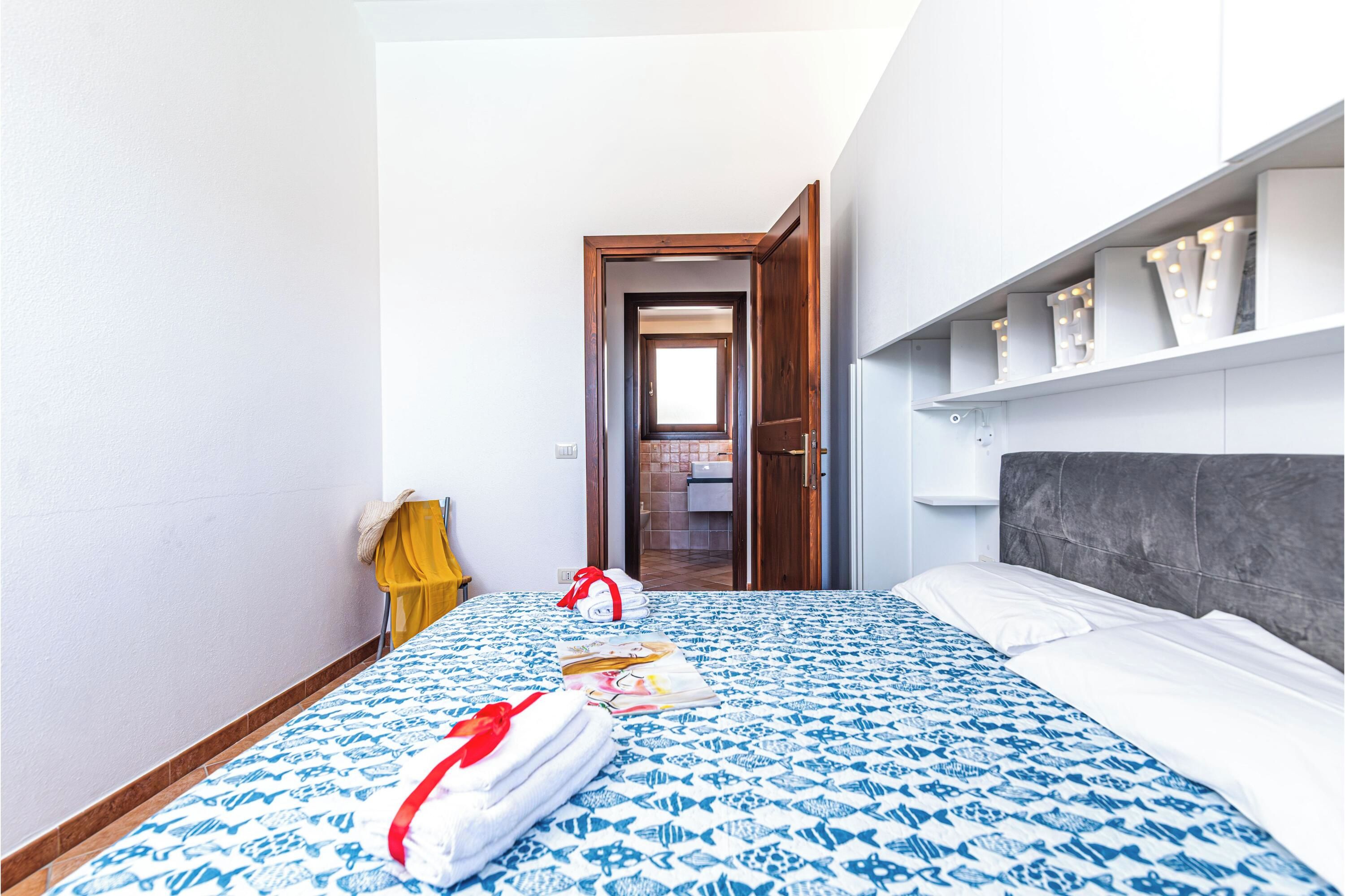 Een hotelkamer met een bed, een badkamer door een open deur zichtbaar, en een plank met decoratieve objecten.