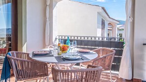 A balcony with a table set for dining, wicker chairs, and a view of the sea. - Vhouse (Badesi)