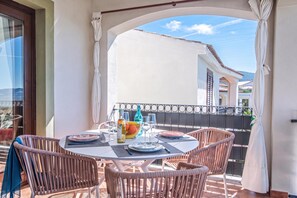 Ein Balkon mit Esstisch, Korbstühlen und Blick auf das Meer.