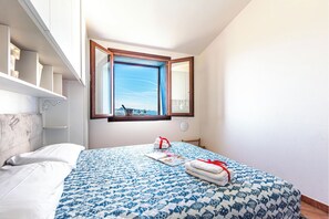 Ein Schlafzimmer mit Bett, Fenster mit Aussicht, Nachttisch und einer an der Wand befestigten Ablage.