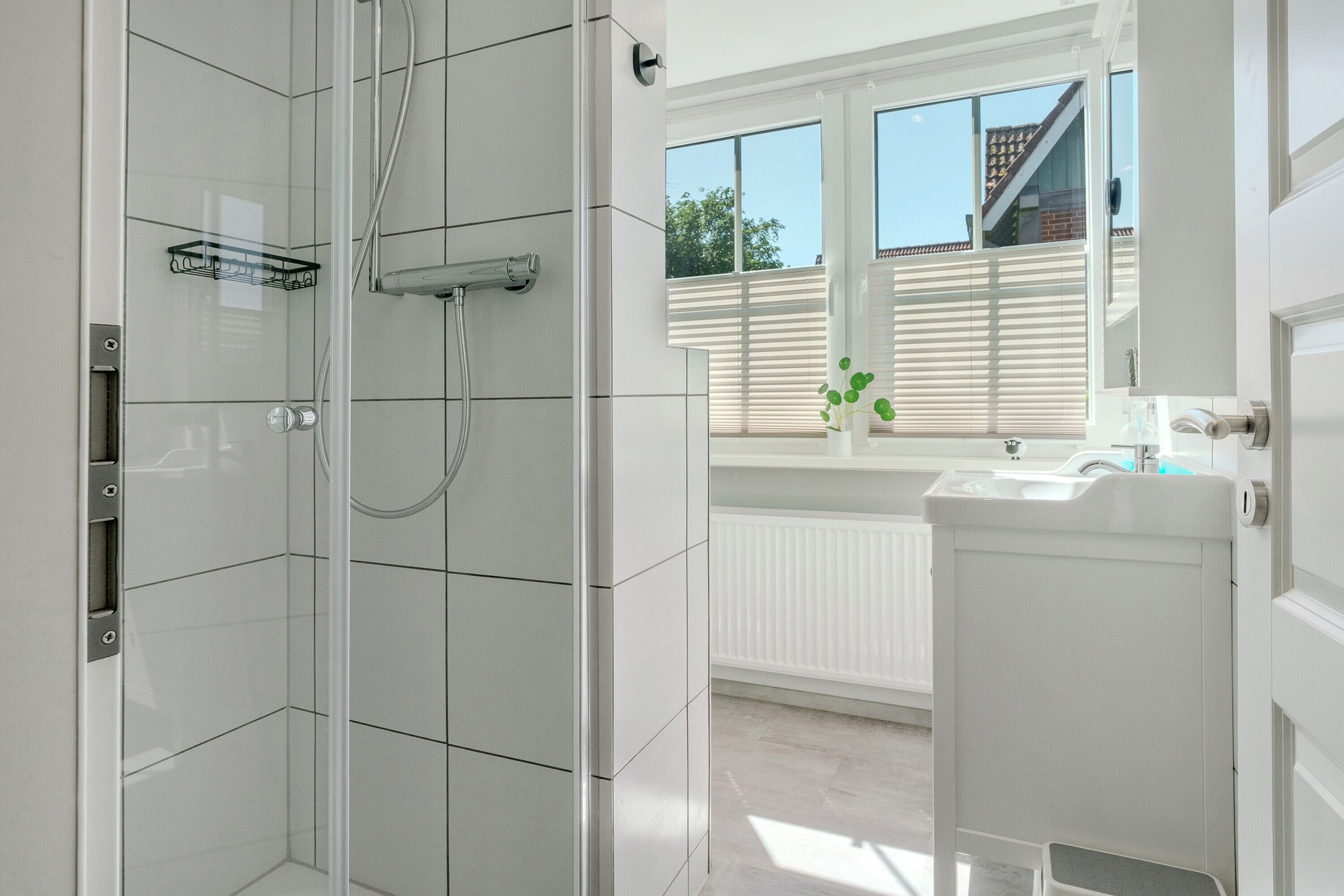 Een badkamer met een douche, wastafel en een raam met zonwering.