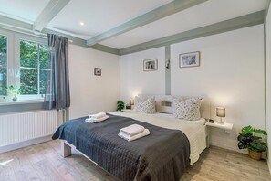 Un dormitorio con cama, mesita de noche, lámpara y ventana con cortinas.