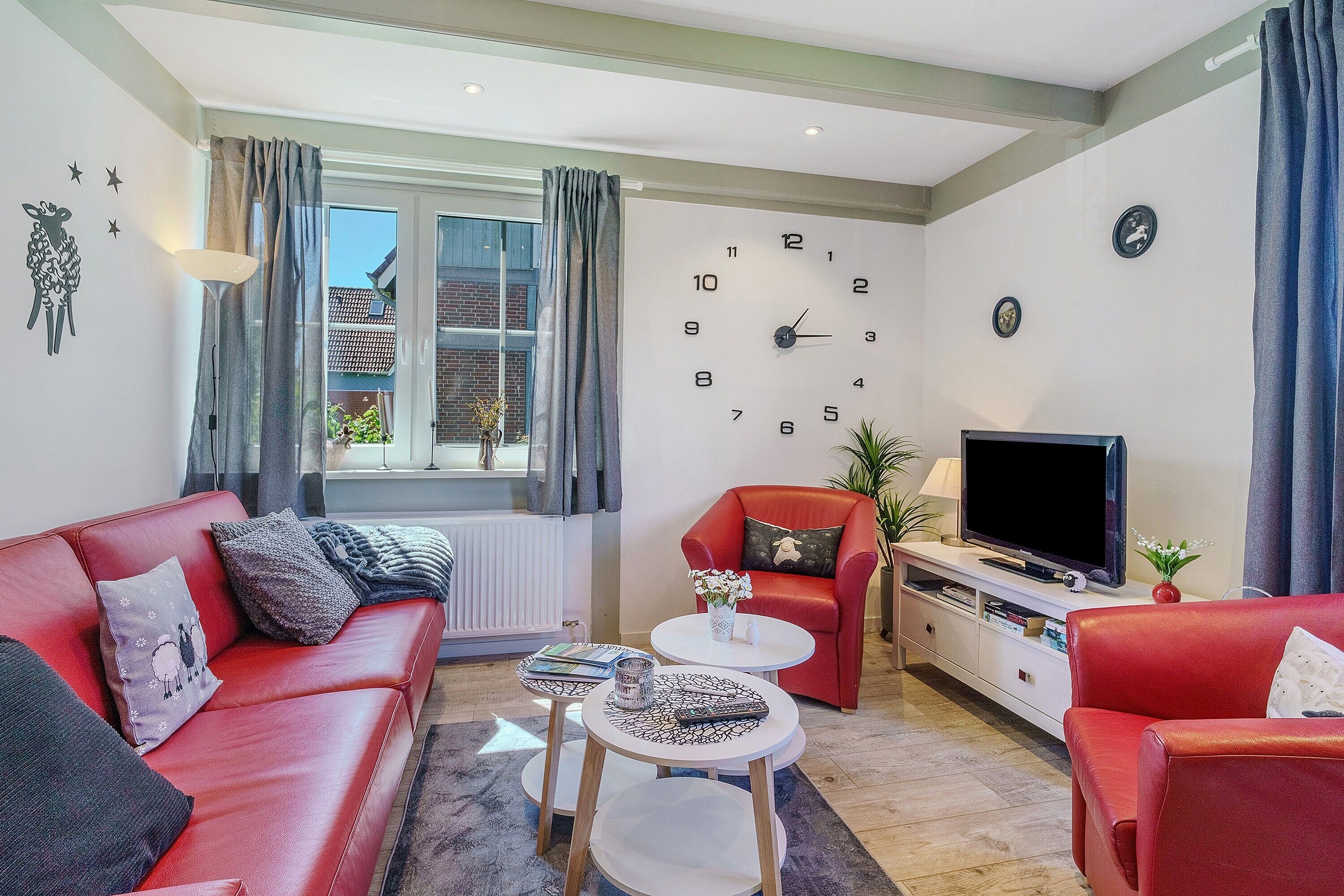 A living room with a red sofa, a red armchair, a coffee table, a TV, and a window with curtains.