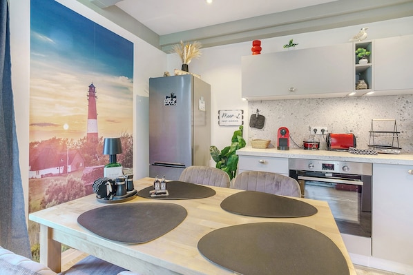 Una cocina moderna con horno empotrado, comedor con mesa y sillas, y un cuadro grande de un faro.