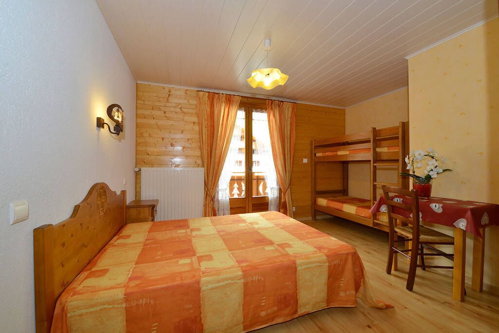 Una habitación con una cama, una litera, una mesa con una silla y una ventana con cortinas.