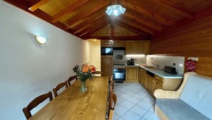 Una mesa de comedor de madera con sillas, un florero con flores, una cocina con armarios de madera, un microondas, una cafetera y un fregadero.