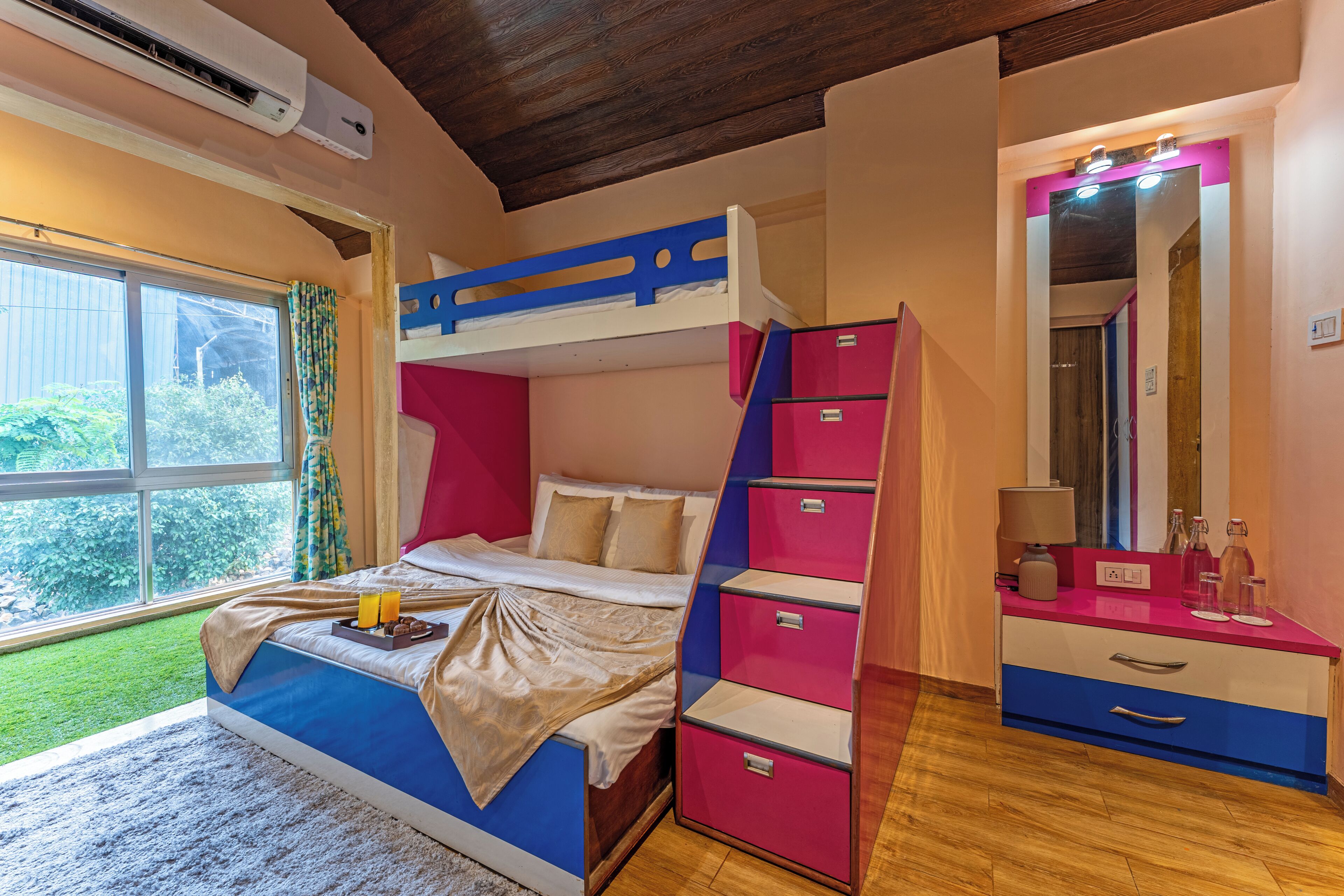 A bedroom with a bunk bed, a dresser, a mirror, and a window with a view of greenery.