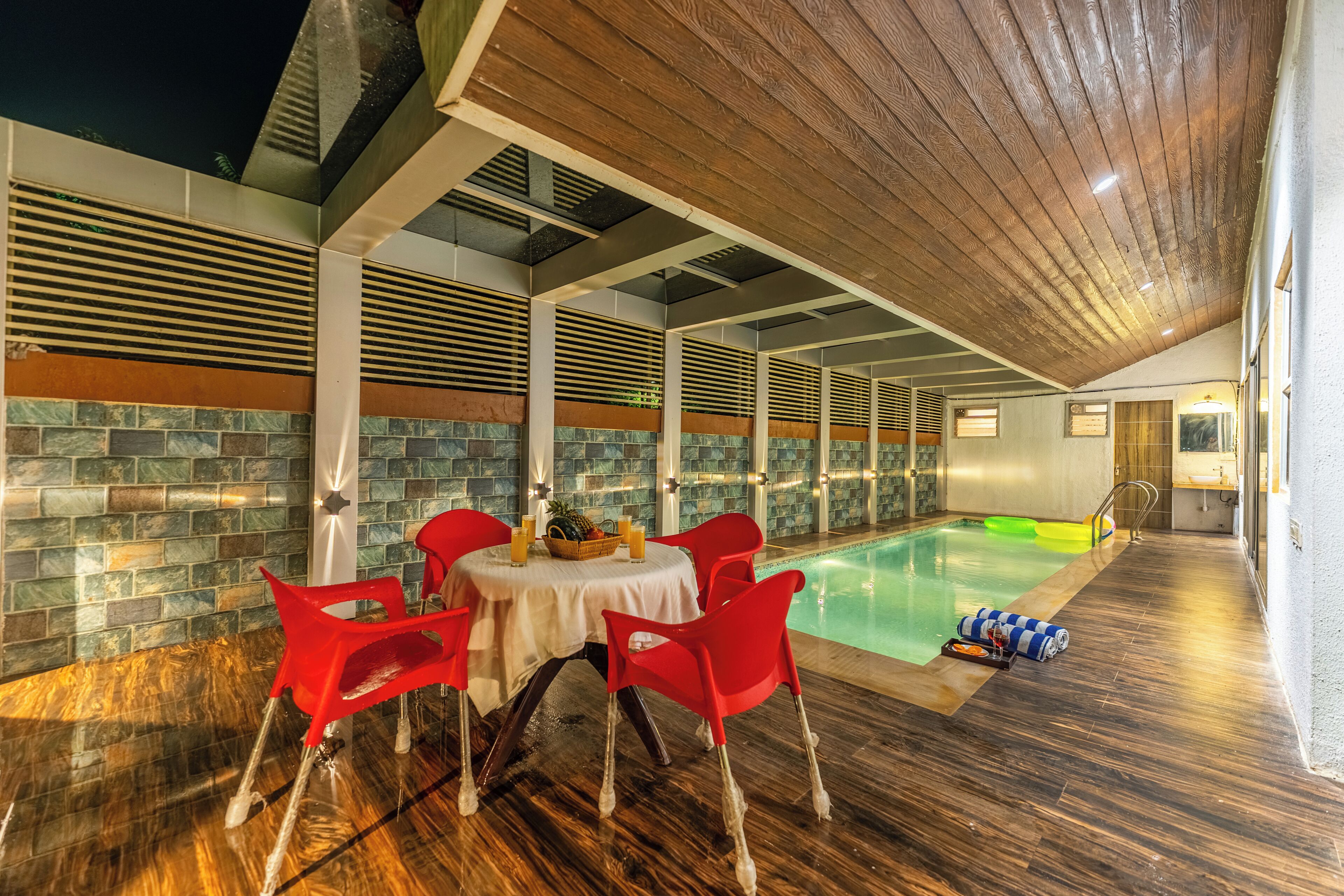 A poolside area with a table and chairs, a pool, and a wooden ceiling.