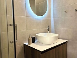 A modern bathroom with a round white sink, a mirror, and a wooden vanity. - Origins III | Modern Seaside Studio in Piso Livadi (Piso Livadi Paros)