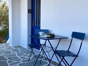 A small outdoor seating area with a table and two chairs, a blue door, and a stone floor. - Origins II | Calm Studio near Beach & Taverns (Piso Livadi Paros)