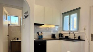 Eine moderne Küche mit weißen Schränken, einem schwarzen Geschirrspüler, einer Kaffeemaschine und einem Fenster mit Jalousien.