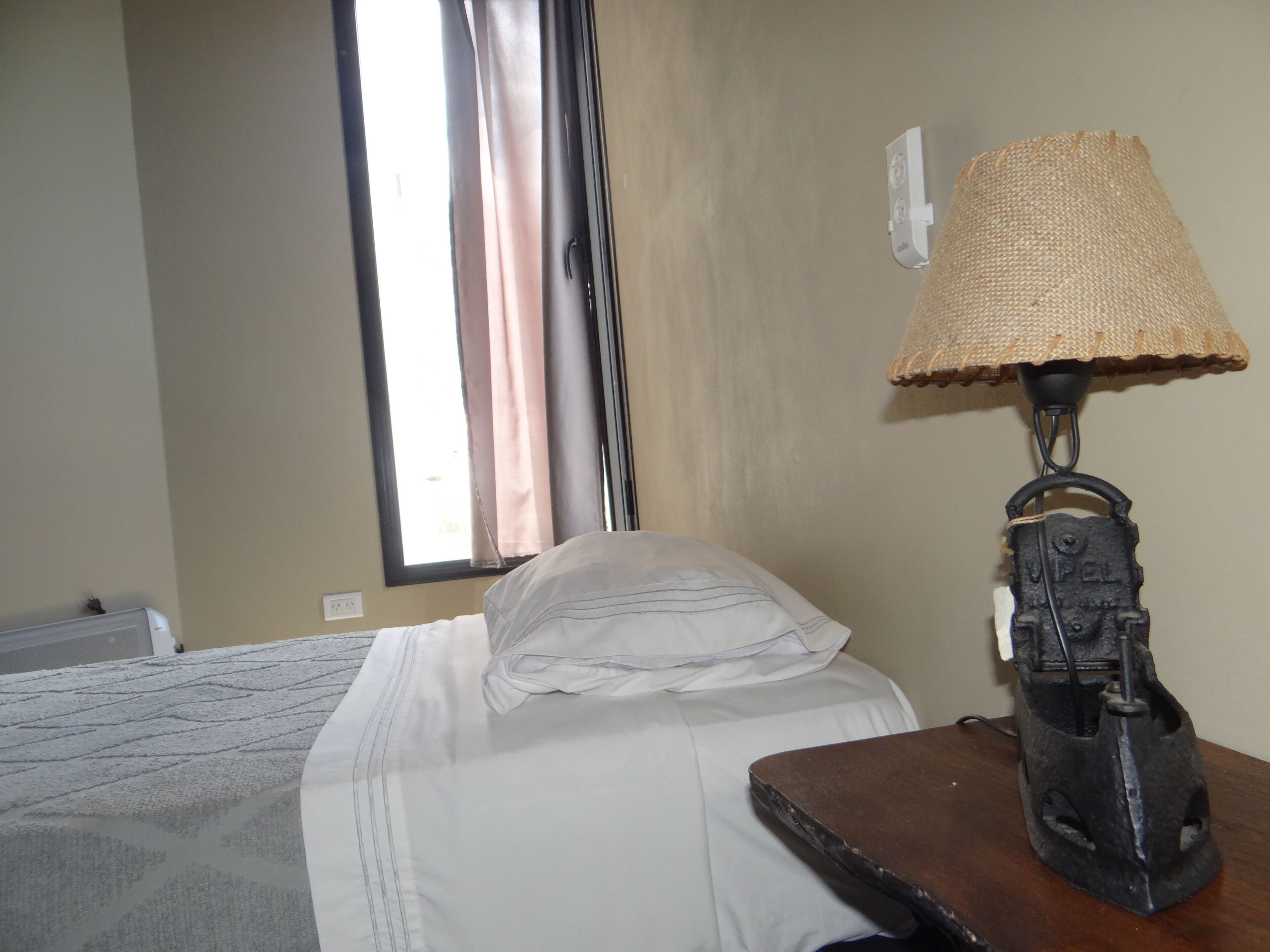Una habitación de hotel con cama, lámpara y ventana con cortinas.