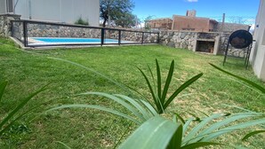 Un jardin avec une piscine, un barbecue et un mur en pierre.
