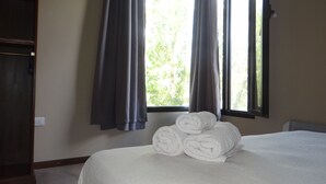 Une chambre avec un lit, une fenêtre avec des rideaux, une armoire et une pile de serviettes.