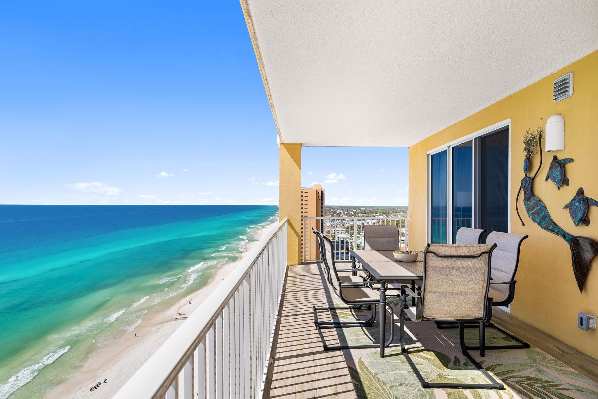 Un balcon avec vue sur la plage et l’océan, une table avec des chaises et un mur décoratif.