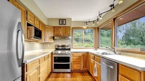 Een moderne keuken met houten kastjes, roestvrijstalen apparatuur en een groot raam met uitzicht op groen.