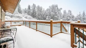 Een sneeuwbedekt terras met houten leuning, een tafel met stoelen en een uitzicht op met sneeuw beladen bomen.
