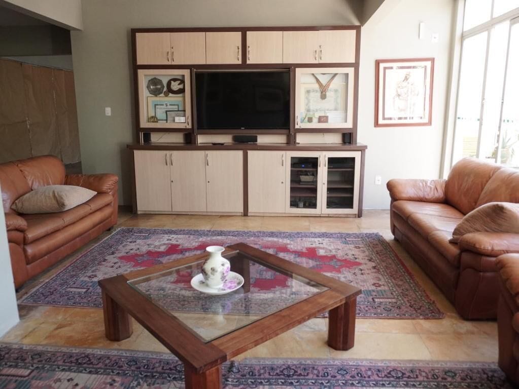 Una sala de estar con un sofá de cuero marrón, una mesa de centro de vidrio, un televisor sobre un mueble bajo y alfombras estampadas.