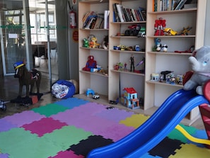 A children's play area with a blue slide, a variety of toys, and bookshelves filled with books and toys.