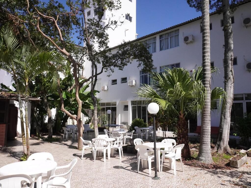 An outdoor seating area with white plastic chairs and tables, surrounded by palm trees and a building with multiple windows.