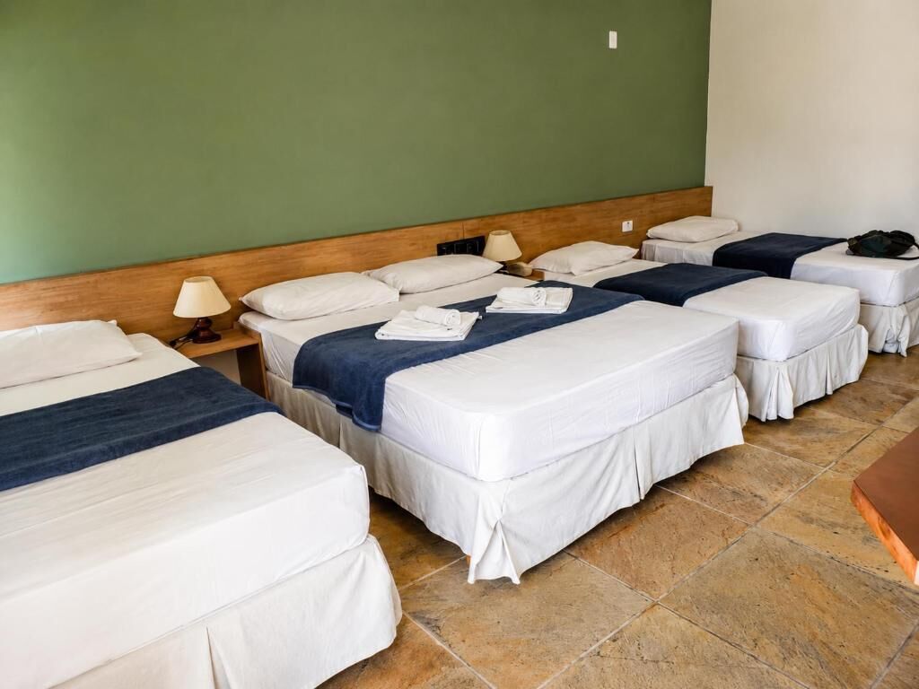 Una camera d'albergo con diversi letti allineati, una testiera in legno e una parete verde.