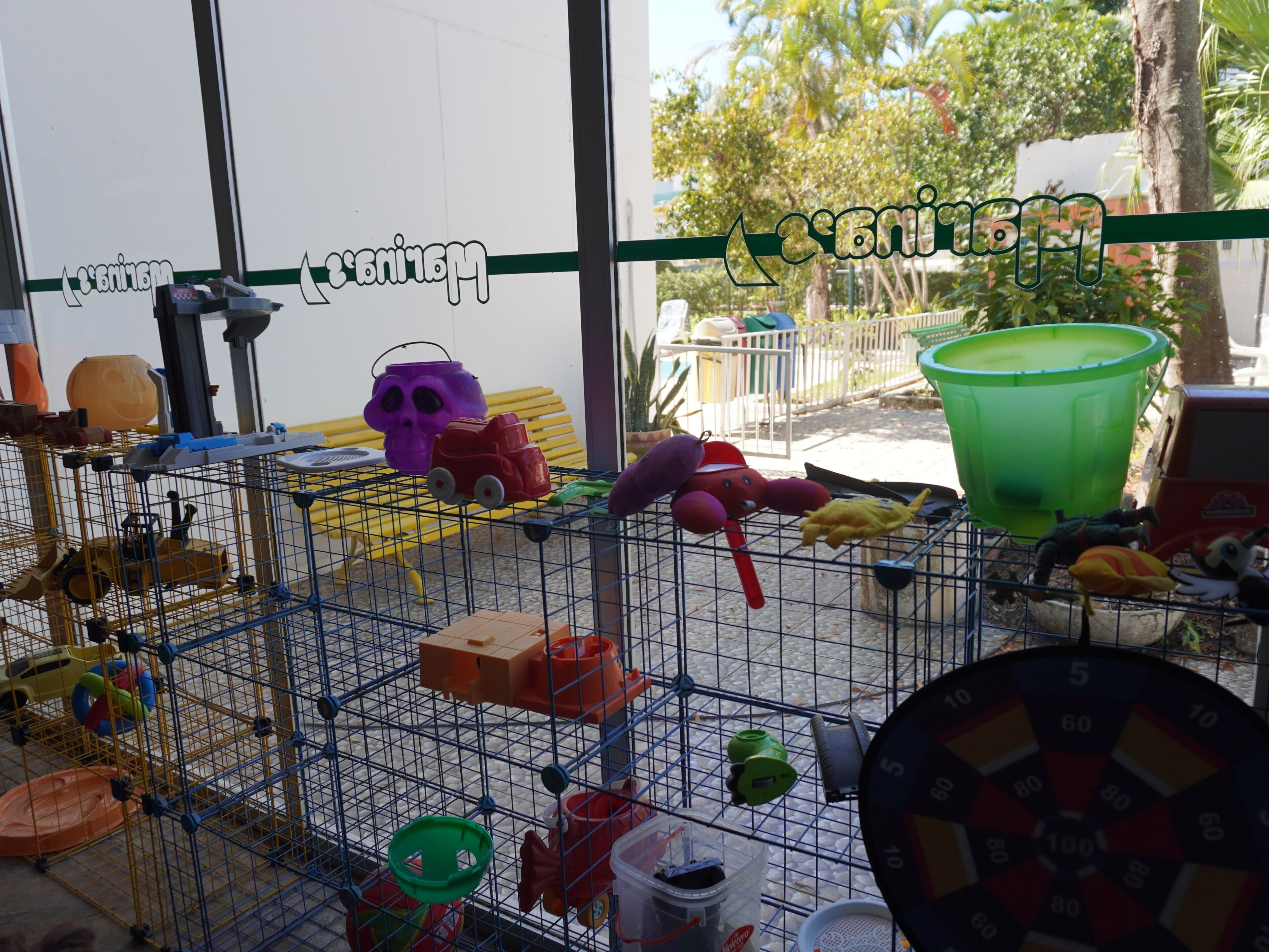 A metal cage with toys and containers, a green bucket, and a dartboard.