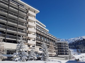 Ein modernes Mehrstöckhotel mit Balkonen in einer verschneiten Berglandschaft.