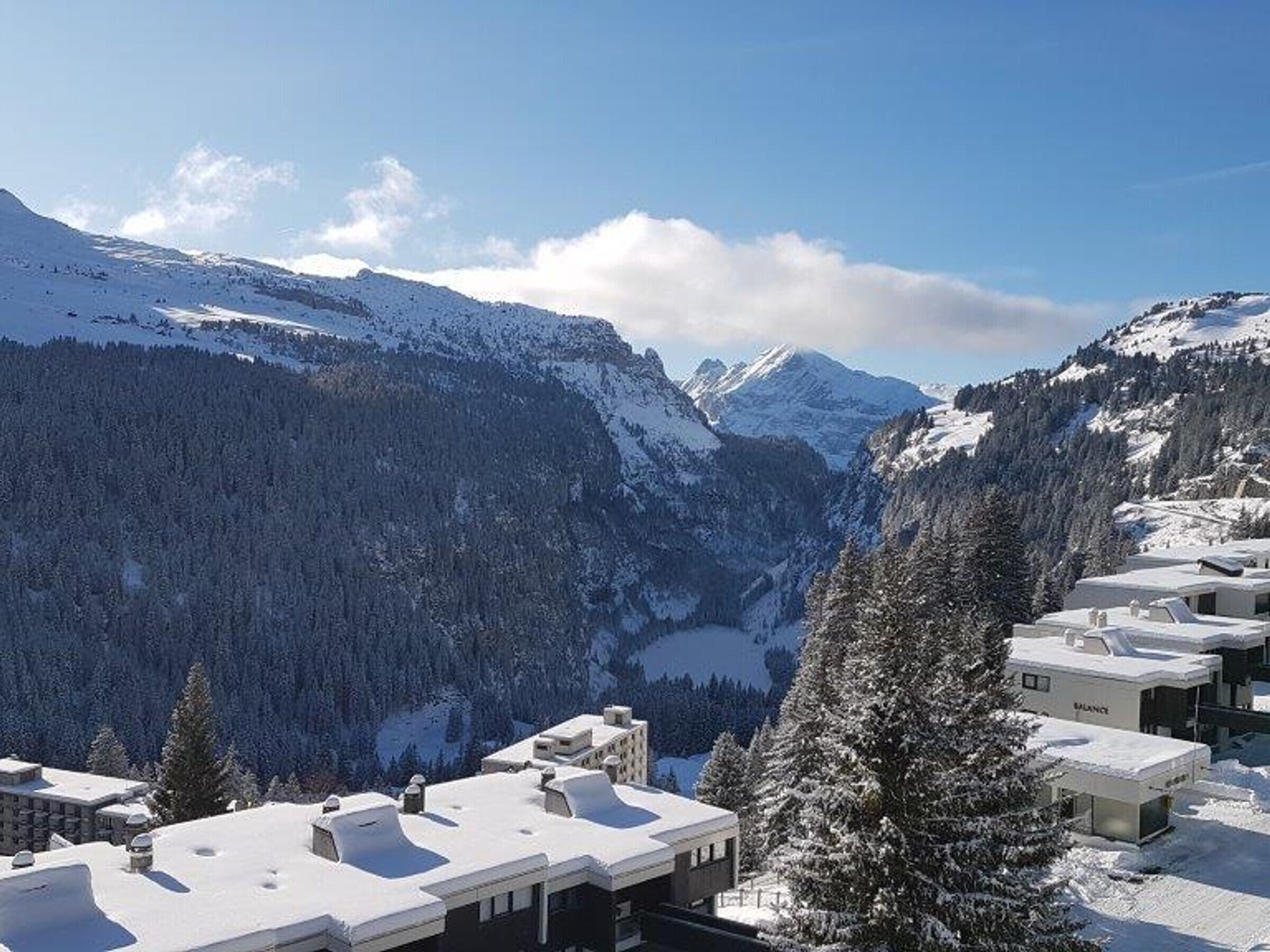 Un paysage montagneux enneigé, avec une vallée et une rangée de bâtiments modernes aux toits plats.