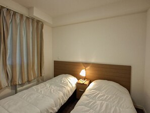 A hotel room with two single beds, a wooden headboard, a bedside table with a lamp, and a window with curtains. - Comfortable apartment - 4 guests (Flaine)