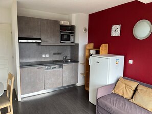 Eine kompakte Küche mit Mikrowelle, Backofen und Geschirrspüler. Neben einer roten Wand mit Uhr und Spiegel steht ein kleiner Kühlschrank.