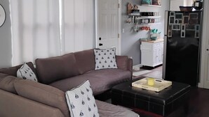 Ein Wohnzimmer mit braunem Sofa, einem Couchtisch, einem Deckenventilator, einem Kühlschrank und einer Tür mit weißem Rahmen.