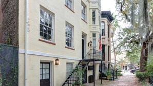A row of townhouses with a central staircase, a flag, and a brick pathway. - The Jones Street Parlor | Historic Retreat (Savannah)