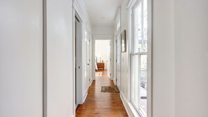 A hallway with white walls, wooden flooring, and large windows. - The Jones Street Parlor | Historic Retreat (Savannah)