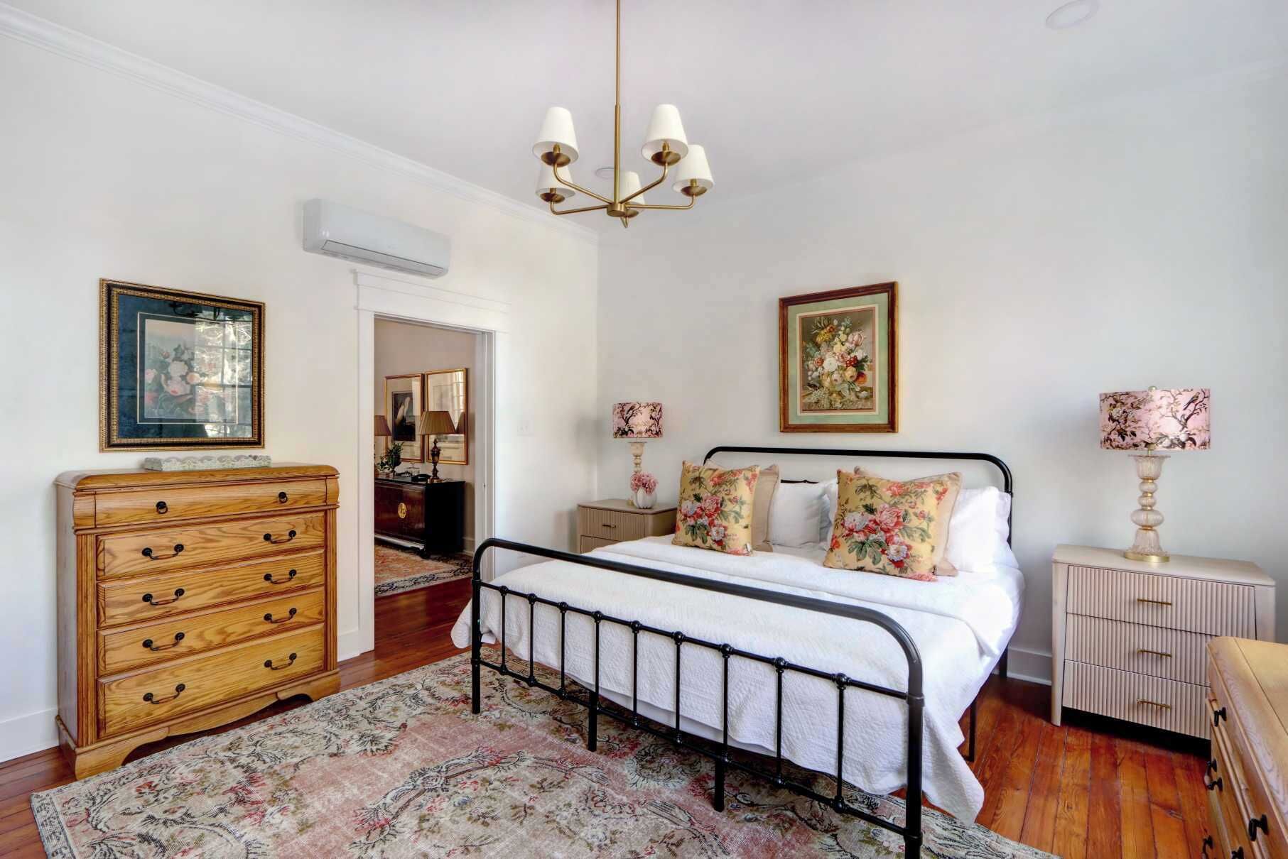 Un dormitorio con cama, cómoda, mesita de noche, lámpara y una obra de arte enmarcada.