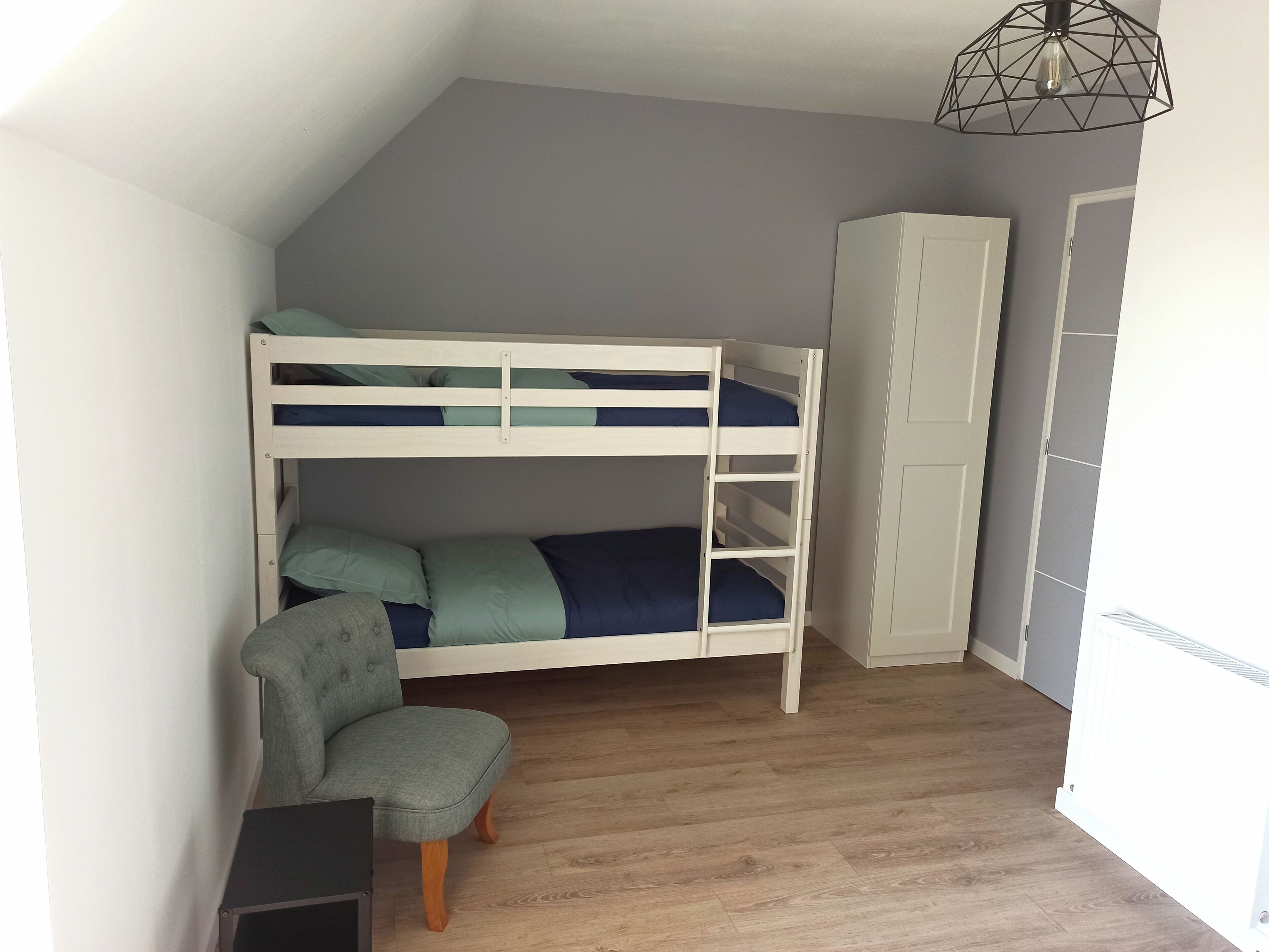 Una cama individual doble con escritorio y silla, un armario y un radiador en una habitación con techos inclinados.