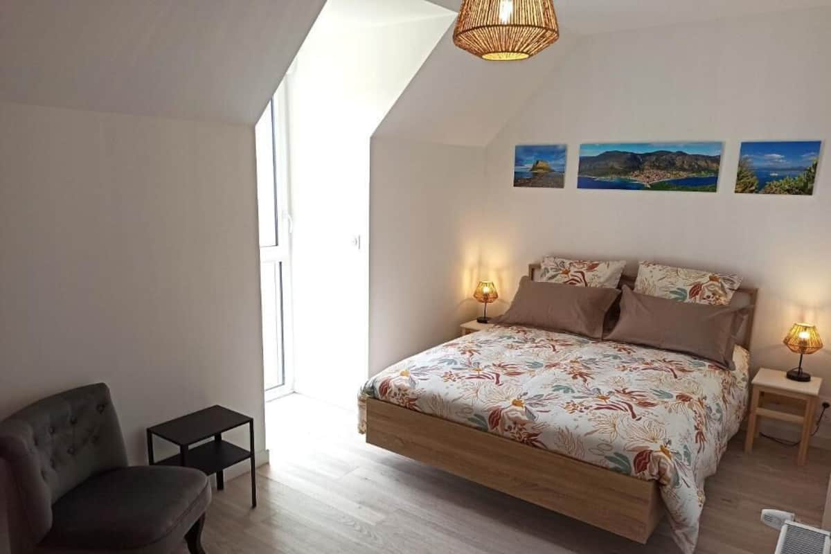 A bedroom with a bed, a chair, a small table, and a heater. There are three paintings on the wall.