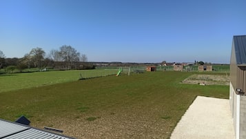 Un campo cubierto de césped con un parque infantil, un edificio pequeño y un granero a lo lejos.