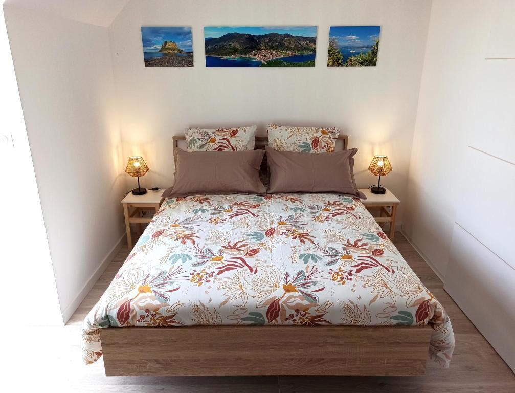 A bed with floral bedding, two bedside lamps, and three landscape paintings on the wall.