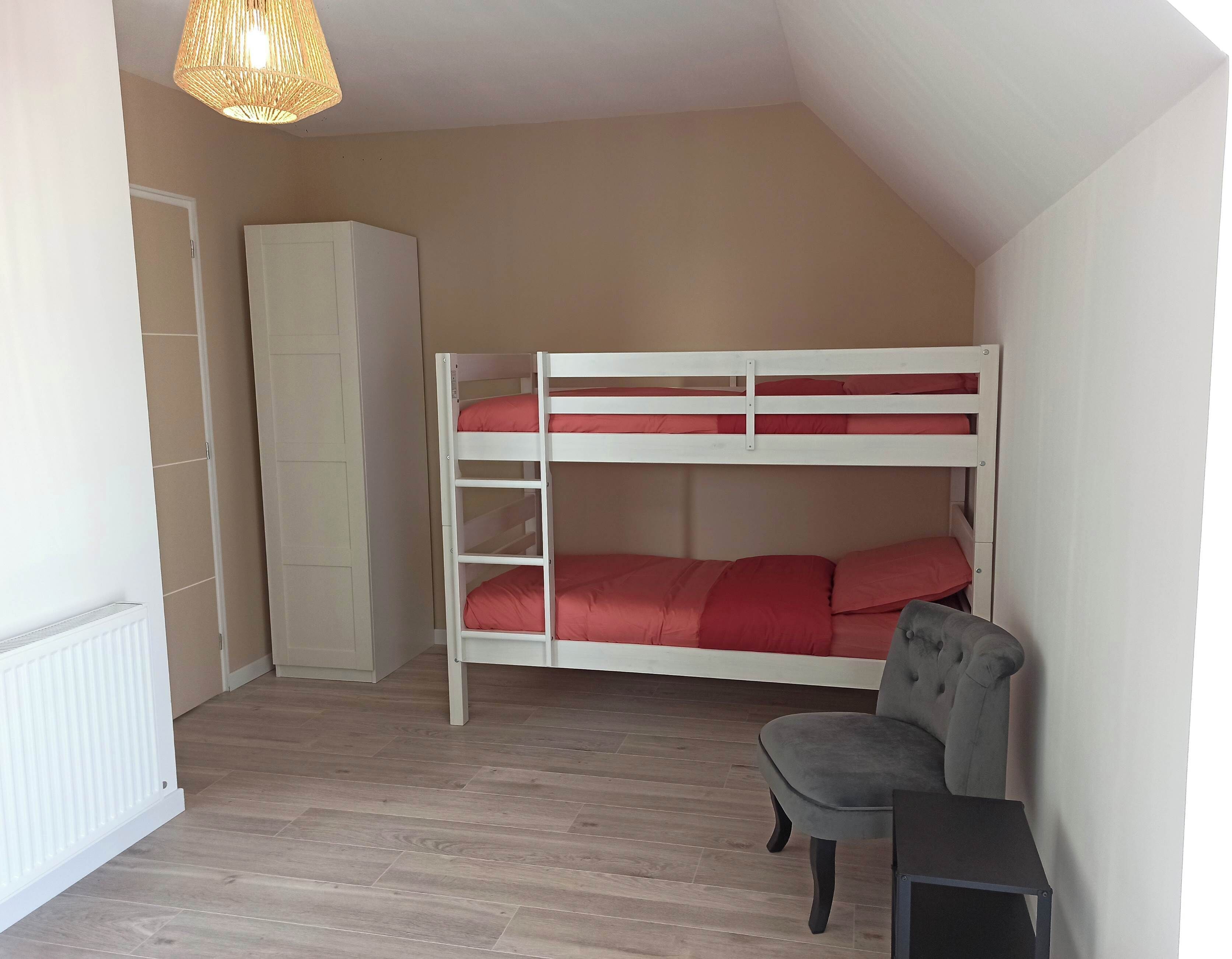 Una stanza con un letto a castello, un armadio, una sedia e un termosifone.
