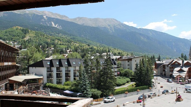 A mountain town with buildings, a parking area, and a view of snow-capped mountains. - Studio for 4 in Serre-Chevalier, Southeast Balcony (Saint-Chaffrey)